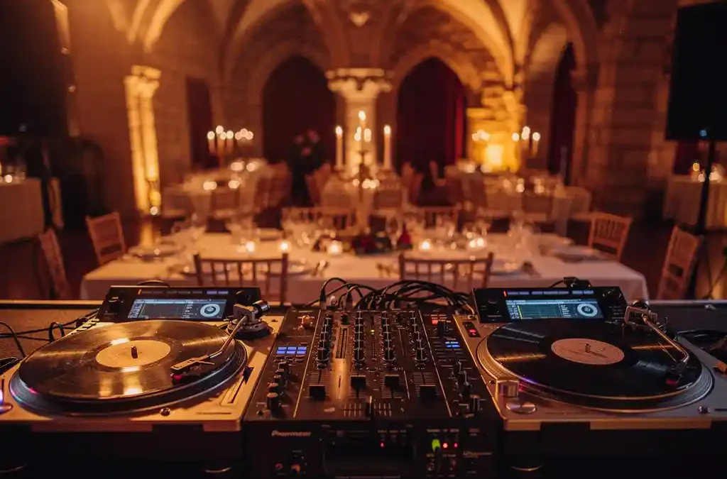 DJ-opstelling met mengpaneel en vinylplaat in verlichte balzaal van Limburgs kasteel, romantisch gedekte trouwtafels op achtergrond.